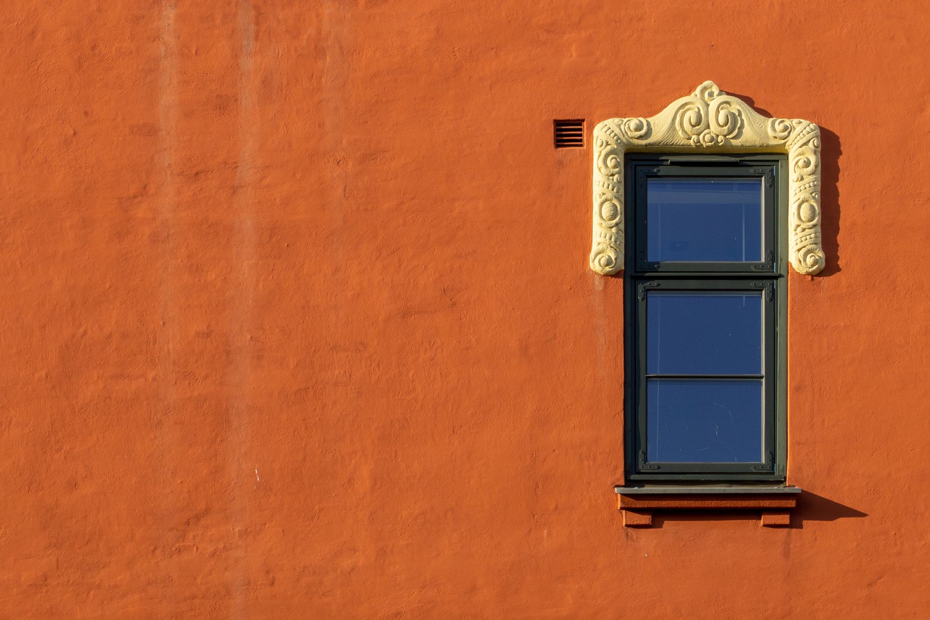 a window on an orange wall with a decorative frame